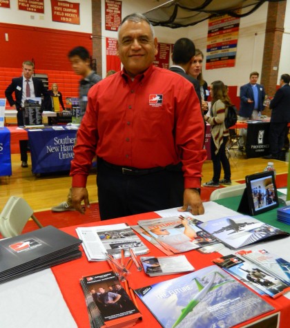 Sam Rath of the National Aviation Academy in Bedford, Mass., stands behind his recruitment materials at the annual College Fair at Watertown High School on Oct. 9, 2014. 